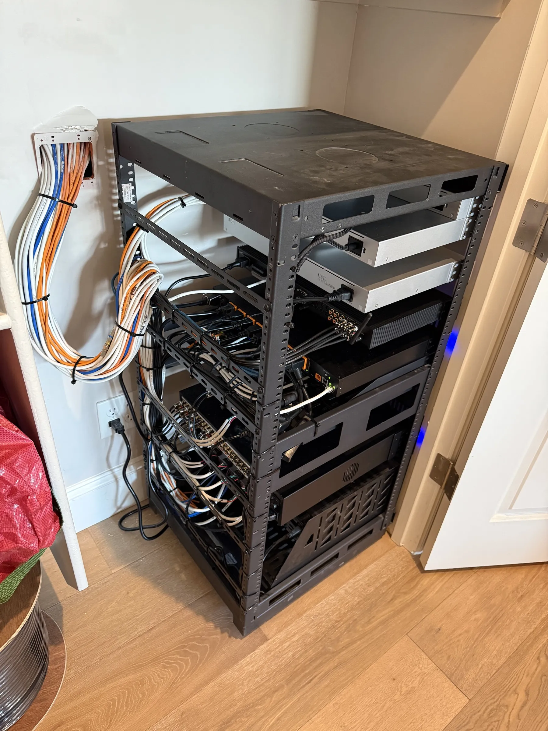 Floor-standing structured wiring equipment rack in a closet, with amplifiers and network gear installed and cabling routed to the side.