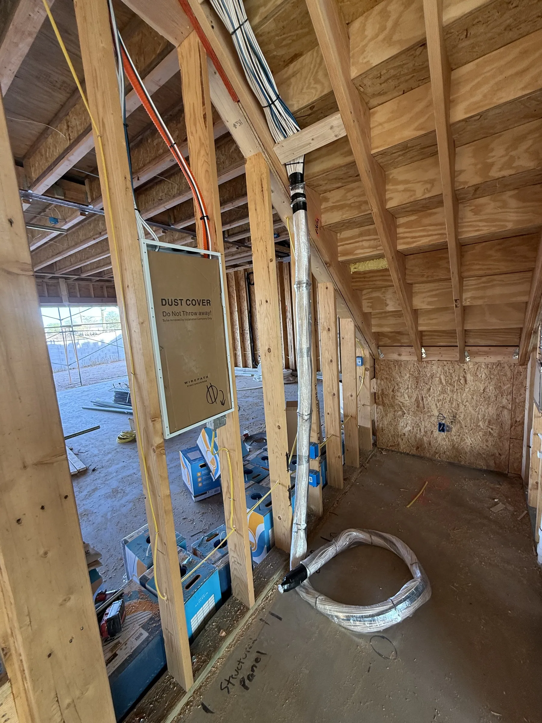 Open attic framing during a new-construction pre-wire, with a labeled dust-cover panel mounted to a stud and structured cable routed along the rafters.