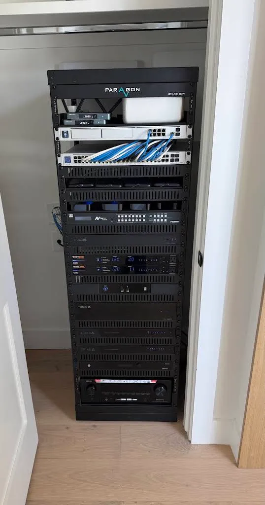 Floor-standing Paragon AV equipment rack with a UniFi network switch, neatly combed Ethernet cabling, WattBox power conditioners, and Triad amplifiers, installed in a home closet.